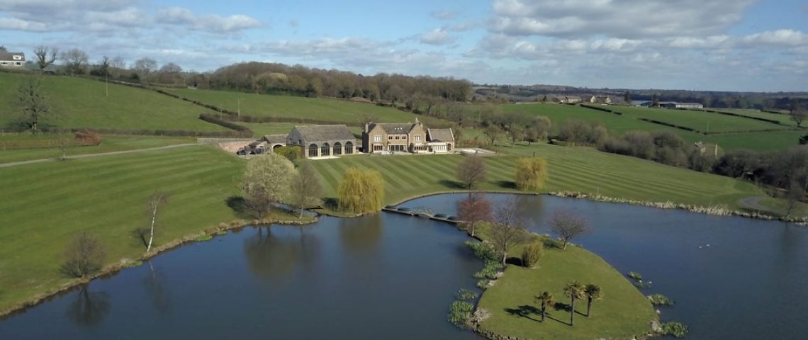 Aerial view of a Derbyshire country house with landscaped grounds and a lake with an island
